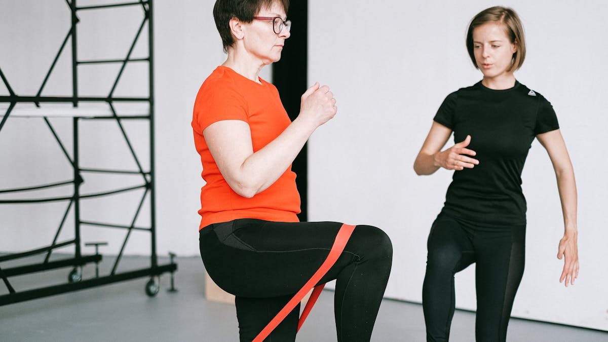Personal trainer guiding a woman with resistance band exercise in a gym setting.